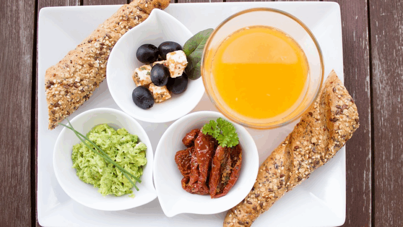 A picture of a breakfast plate with bread, vegetables and juice.