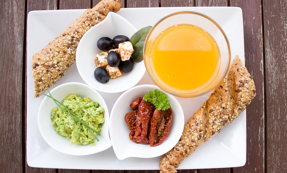A picture of a breakfast plate with bread, vegetables and juice.