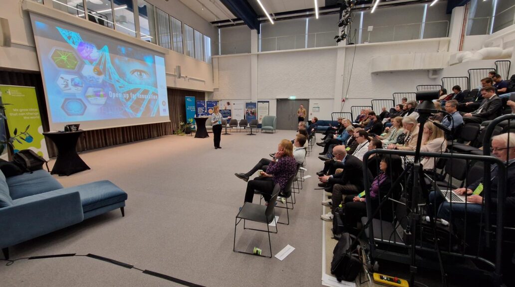 A picture of a room filled with people and a person on stage talking.