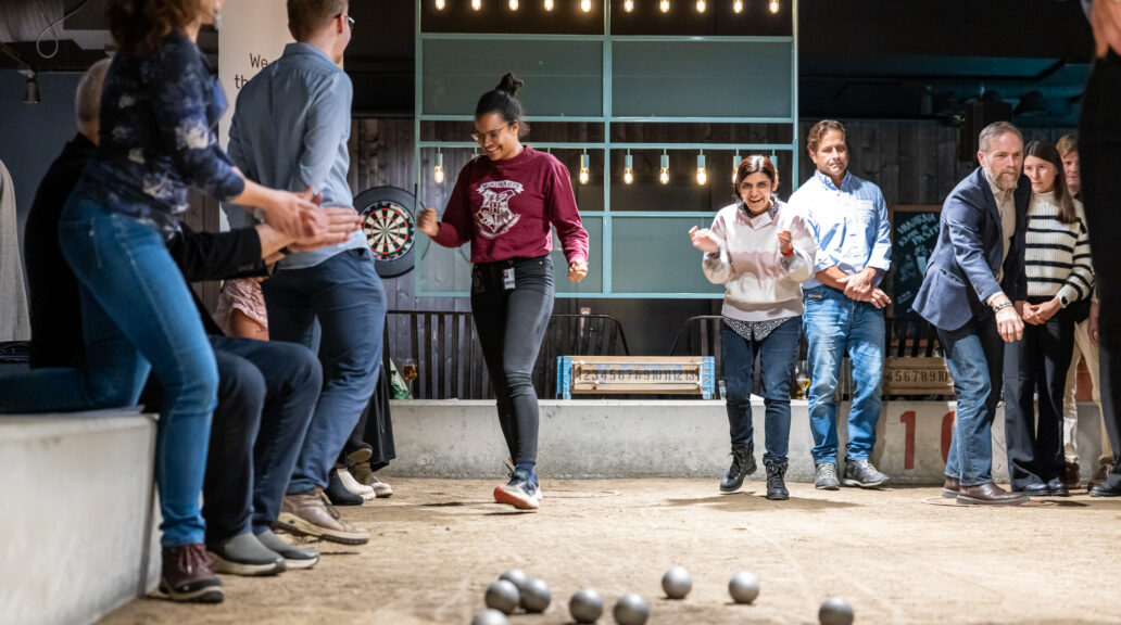 People playing boule inside. One woman is happy and clapping her hands after a good throw.