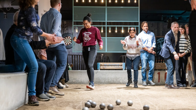 People playing boule inside. One woman is happy and clapping her hands after a good throw.
