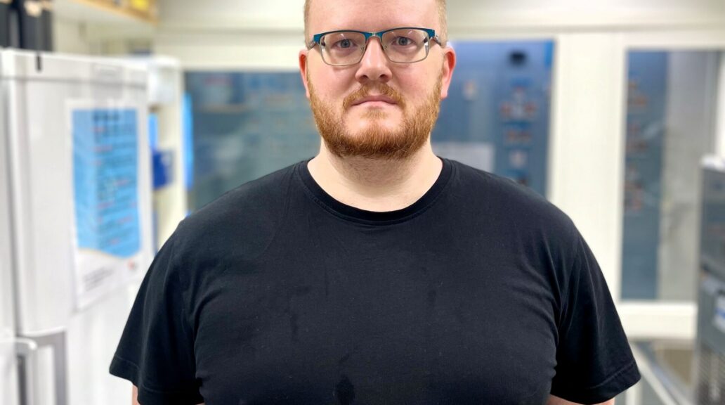 A picture of Björn Greijer, a man in his 30's wearing glasses, in a lab.