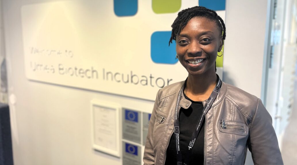 Ololade Awoyomi in the UBI facilities. She's wearing a grey jacket and a black shirt, in front of the Umeå Biotech Incubator logotype.